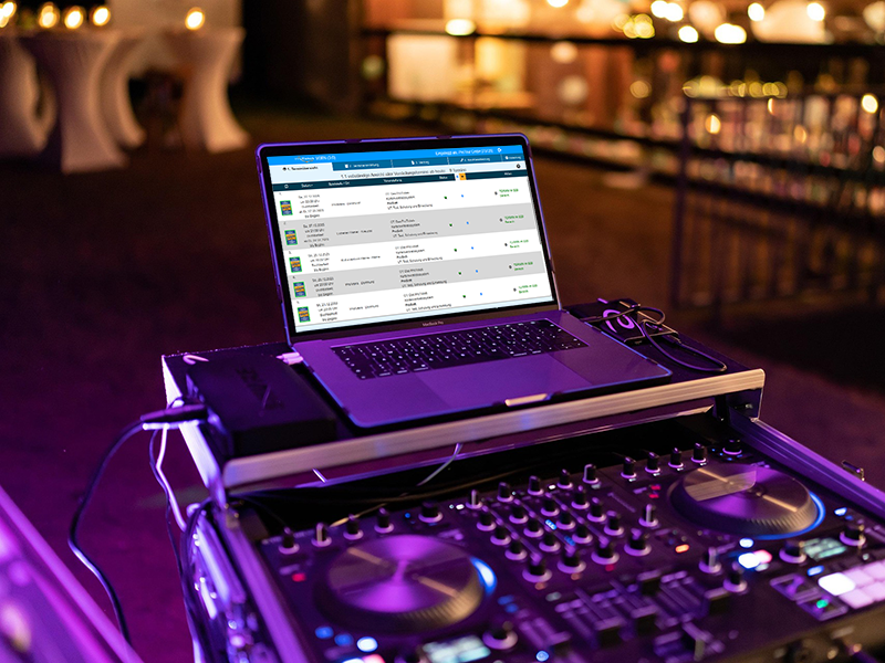 Ein MacBook, der die VGen Seite zur Veranstaltungseinrichtung von ProTicket geöffnet hat und auf einem DJ-Setup steht, welcher für eine Bühne zur Zeit aufgebaut wird
